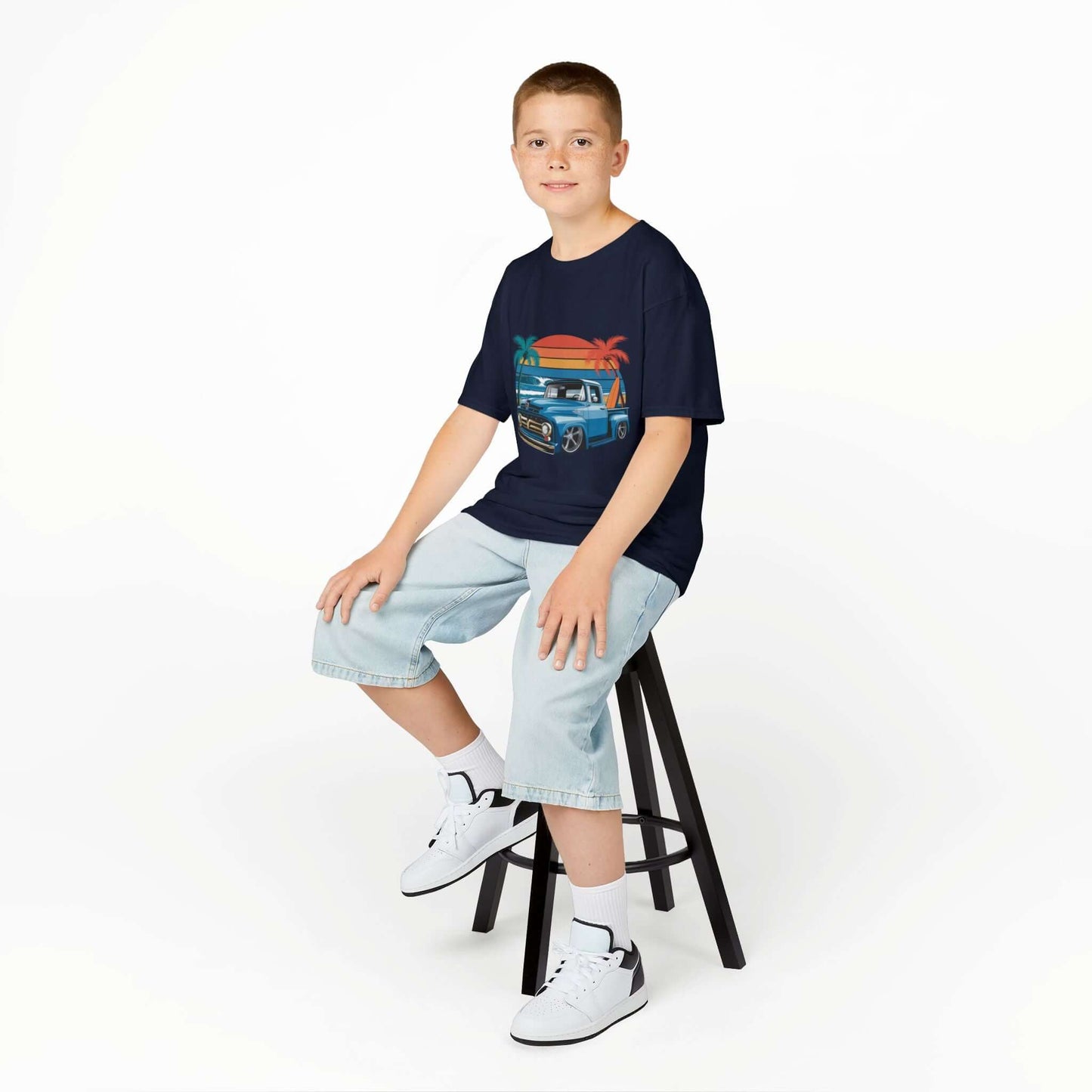Boy sitting on a stool wearing a retro kids t-shirt with vintage pickup truck design, perfect for car lovers.