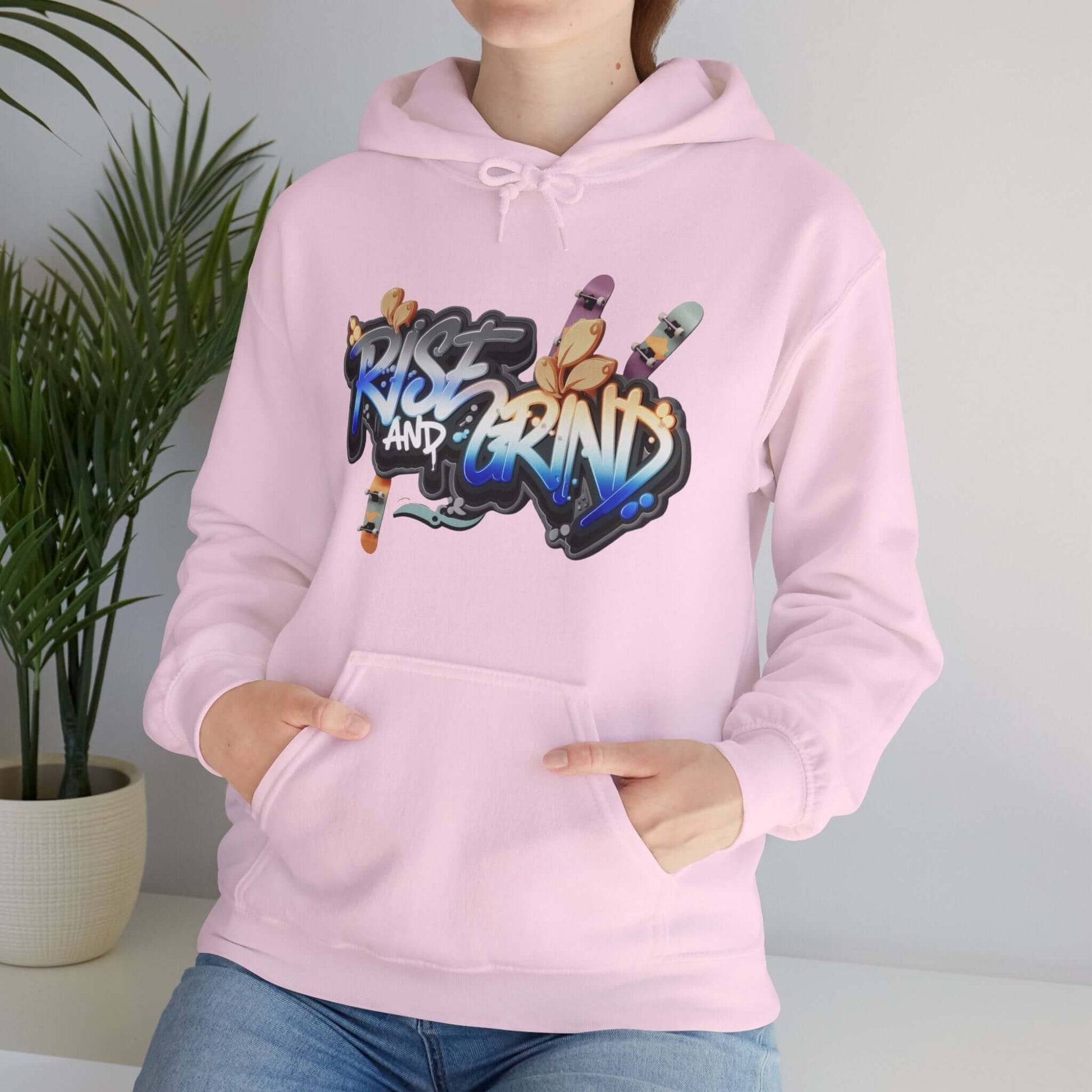 Unisex pink hoodie with 'Rise and Grind' graffiti design featuring skateboards, perfect for streetwear enthusiasts.