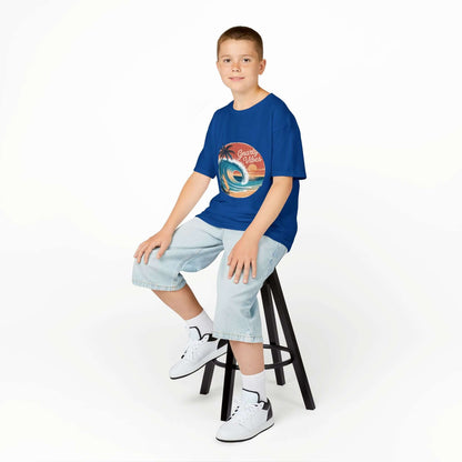 Boy wearing a blue Kids Tee with retro surf design, sitting on a stool, showcasing summer beach vibes.