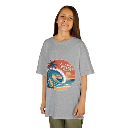 Kids tee with retro big wave surf design and 'Gnarly Vibes' on a sunset beach backdrop.
